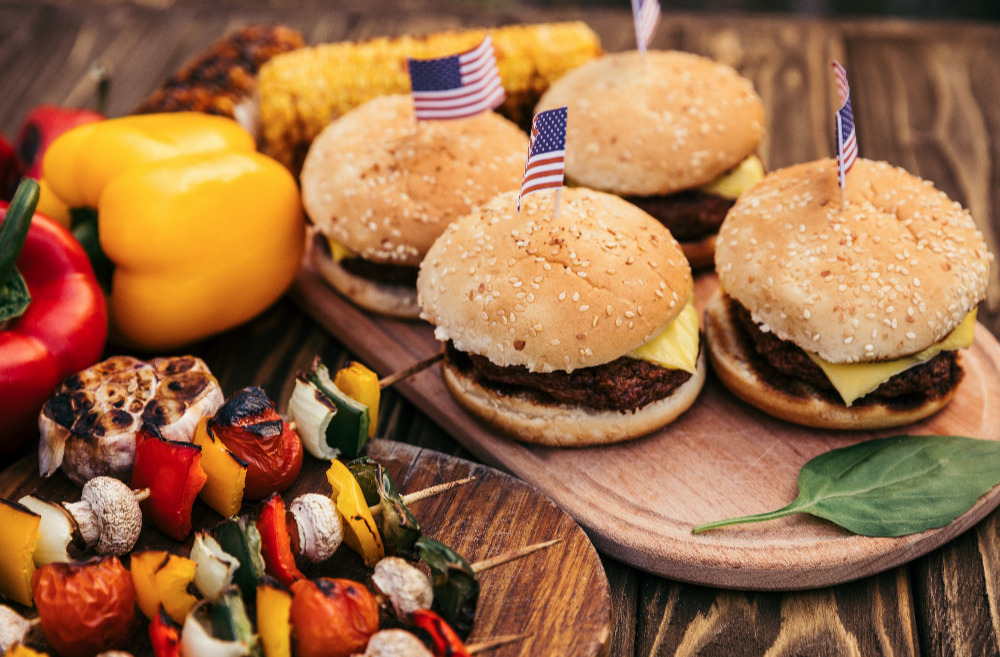 Grilled skewers and hamburgers with American flags on a wooden table